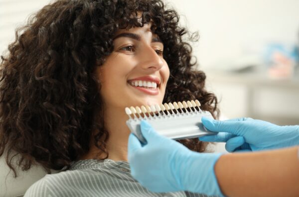 Doctor checking young woman's teeth color in clinic, closeup. Dental veneers
