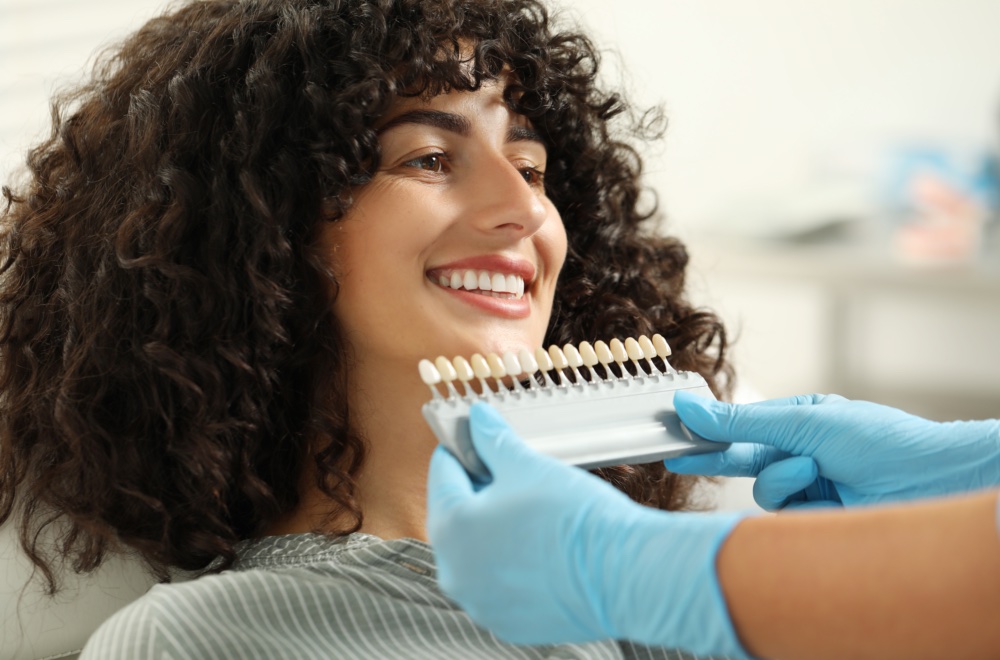 Doctor checking young woman's teeth color in clinic, closeup. Dental veneers